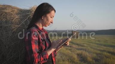 农民依靠干草，用<strong>平板</strong>电脑在麦田上。 女农民在干草堆旁边的田里使用<strong>平板</strong>电脑。 <strong>微笑</strong>